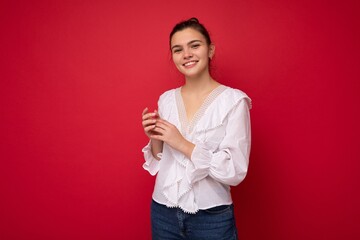 Portrait of positive cheerful fashionable woman in formalwear holding two hands together looking at camera isolated on red background with copy and empty space