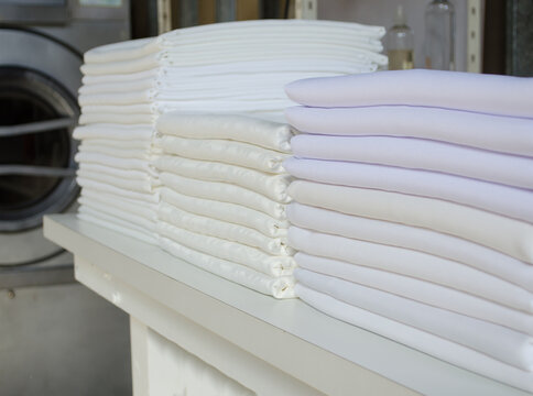 Stack of folded white fabrics, bed sheets, tablecloths in an industrial laundry.