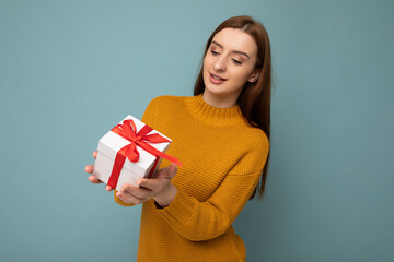 Shot of attractive positive smiling young brunette woman isolated over colourful background wall wearing everyday trendy outfit holding gift box and looking to the side