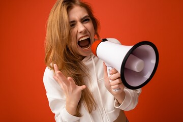 Photo portrait of beautiful pretty angry dissatisfied emotional dark blonde young woman with sincere emotions wearing hipster white hoodie isolated over orange background with copy space and screaming