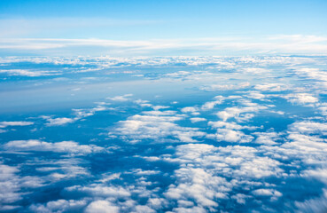 Fototapeta na wymiar Airplane window view of clouds and blue sky from high altitude during air travel