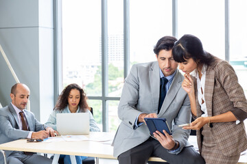 Businessman and businesswoman sharing laptop while standing in office building room.
