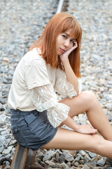 A beautiful Asian woman with short hair looking forward sitting on the railroad tracks.