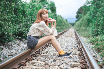 A beautiful Asian woman with short hair looking forward sitting on the railroad tracks.