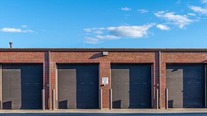 Maintenance bay garage doors on a brick building.  The sky above is an a sunny day with some white cumulus clouds visible.