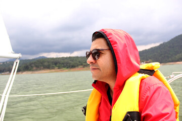 Latin adult man with sunglasses relaxed and happy with life jacket drives a sailboat on the lake...