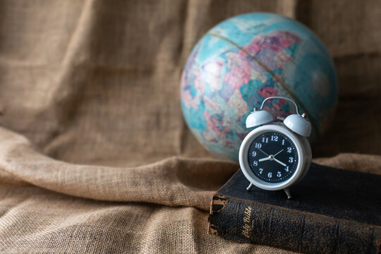 Close up of alarm clock on the old holy bible with blurred world globe on vintage linen sackcloth background against, copy space, Christian background, bible study or the world end time concept.