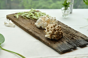 White and black Agrocybe cylindracea or Yanagi Matsutake mushrooms put on a wooden slab placed on a white table. Scientific name that Agrocybe cylindracea is a species imported from Japan. 

