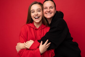 Photo shot of attractive positive smiling brunette female teenager wearing stylish red hoodie and...
