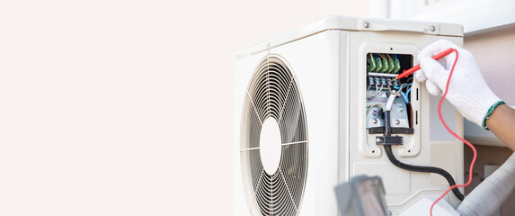 Technician Air-conditioning repairman using measuring equipment checking electric at circuit breaker on outdoor air compressor unit after install and check refrigerant system maintenance.