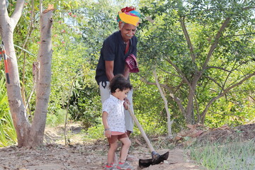 Indian grandfather younger grandson working in the garden with a shovel and younger grandson...