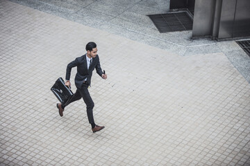 Young businessman with a briefcase running in the urban city street because he is late for his business appointment.
