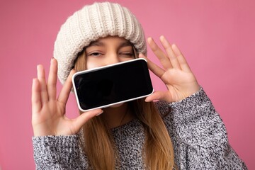 Closeup photo of winking Beautiful young blonde woman wearing casual grey sweater and beige hat...