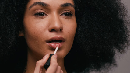 close up of african american woman applying lip gloss isolated on grey