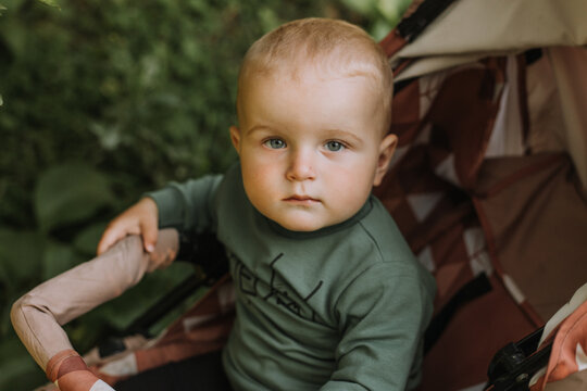 closeup portrait of a baby boy in a green sweater sitting in a stroller. High quality photo