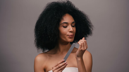 Obraz premium young african american woman holding nail file and blowing on nails isolated on grey