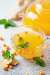 Hot autumn tea with sea buckthorn, ginger and mint in a glass teapot on a gray background