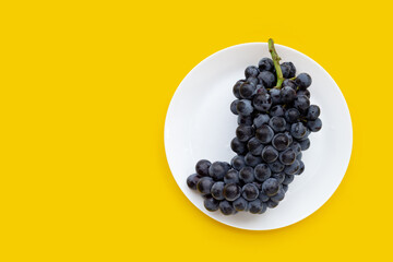 Fresh black grapes in white plate on yellow background.