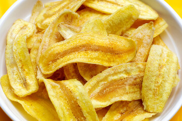 Banana slice chips in white plate on yellow background