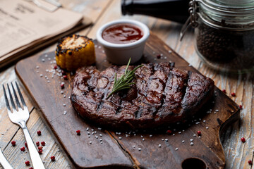 Juicy buffalo steak with grill traces and baked corn,on a dark wooden cutting board