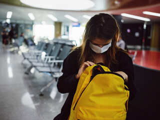 Fototapeta na wymiar a passenger in a medical mask at the airport looks into a yellow backpack