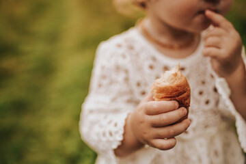 little girl eating croissant in park