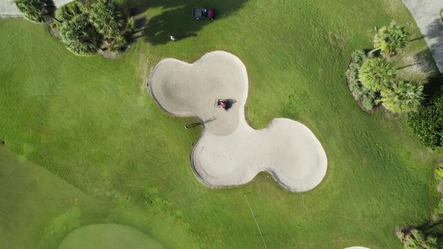 Aerial drone shot of golf course bunker being raked by landscaping crew. Sand bunker maintenance.