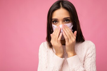 Young beautiful woman in reusable virus protective mask on face against coronavirus and afraiding of isolated on the pink background wall