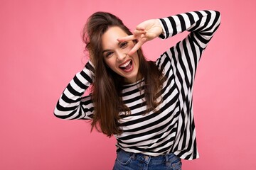 Photo of young european positive smiling winsome joyful happy beautiful brunette woman with sincere emotions wearing casual striped pullover isolated on pink background with copy space