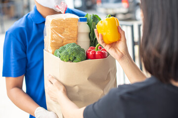 food delivery service man with protection face mask in blue uniform holding fresh food set bag to customer at door home, express delivery, quarantine, virus outbreak, takeaway food delivery concept