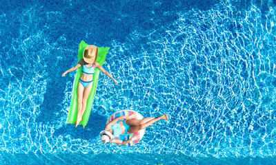 Children in swimming pool aerial drone view from above, happy kids swim on inflatable ring donut and mattress, active girls have fun in water on family vacation on holiday resort
