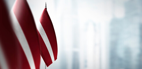 Small flags of Latvia on a blurry background of the city - obrazy, fototapety, plakaty