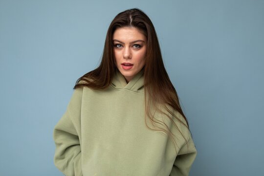Shot of charming young brunet cool female person in a stylish khaki hoodie isolated on blue background. Free space