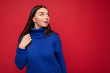 Fototapeta premium Portrait of positive winsome young attractive brunette woman with sincere emotions wearing trendy bright blue pullover isolated over red background with free space