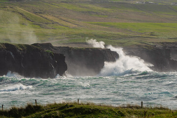 Powerful waves crushing against Cliffs and rough stone coastline of West coast of Ireland. Doolin area. County Clare. Ocean power and rugged Irish coastline. Green fields in the background