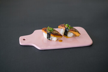 Japanese Sushi - Two Unagi Nigiri Sushi on light-pink board. Sushi pieces served on ight-pin slate isolated on black background. Sushi with backed eel
