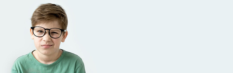 Fototapeta premium Surprised boy in a green T-shirt and glasses pensive scratches his head. Copy space.