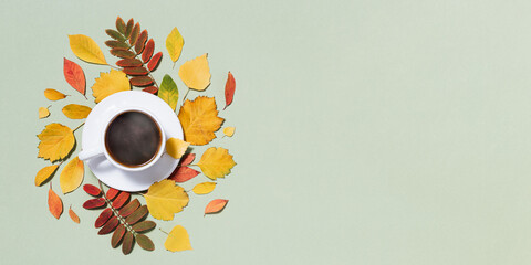 Cup of coffee steaming and red yellow autumn leaves on pastel green Autumn, fall composition