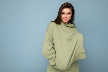 Fototapeta premium Photo of beautiful young brunette cool woman in a stylish khaki hoodie isolated on blue background. Mockup. Empty space