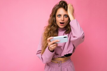 Photo of attractive crazy amazed surprised young woman wearing casual stylish clothes standing isolated over background with copy space holding and using mobile phone looking at camera