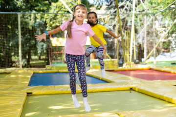 two girls jumping on a trampoline on a summer day.