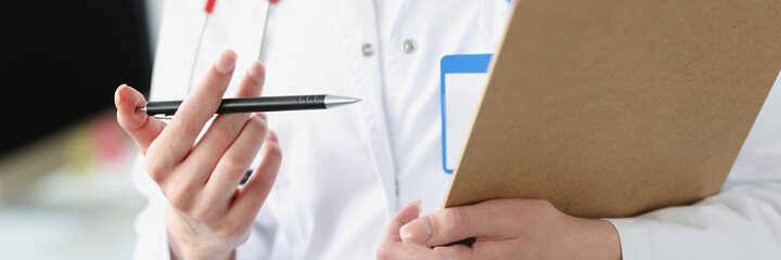 Doctor holding clipboard with documents and ballpoint pen in his hands closeup