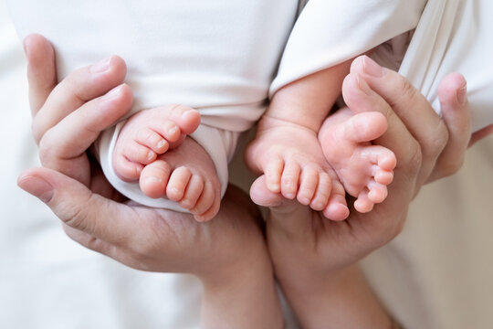 Mom And Dad Hands Hold Small Legs Of Their Two Newborn Twin Babies