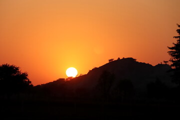 Bright full sun in the evening passing behind the silhouette hills and silhouette trees standing in the forest, sunset view through clean and pure environment and atmosphere of the village