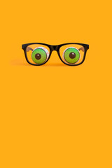 Minimal funny Halloween concept with eyeglasses and doll eyeballs on orange background