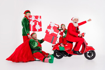 Photo of four teammates people ride scooter sleigh hold sack gifts wear santa elf costume isolated grey color background