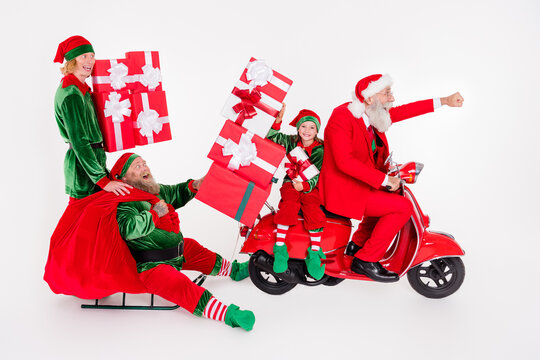 Photo of four excited people ride moped sleigh deliver bag wear santa elf costume isolated white color background
