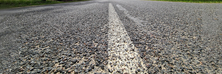 White dividing strip painted on asphalt road against background of trees and blue sky