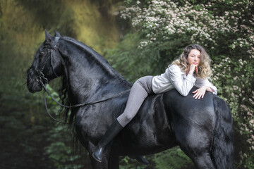 Beautiful young lady posing with a purebred friasian horse in the forest. - 459062535