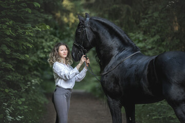 Beautiful young lady posing with a purebred friasian horse in the forest. - 459062539